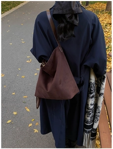 Outdoor shot of a large brown suede tote bag styled with a navy trench coat