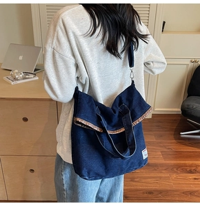 Detail of blue denim tote bag with leather trim and wide strap on model