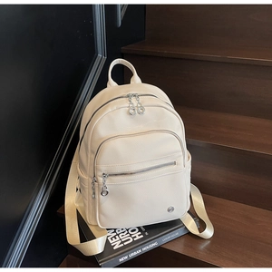 Detail view of beige lychee textured PU leather backpack on a dark wooden staircase