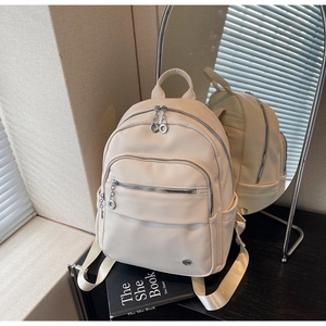 Detail view of the cream-colored faux leather backpack reflected in a stylish oval mirror