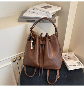 Detail of dark brown leather bucket bag with drawstring closure and beaded charm