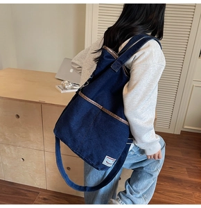 Detail of blue denim tote bag with brown leather trim shown in daily life office setting