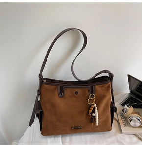 Detail of a brown suede tote bag featuring contrast stitching and a wooden bead tassel
