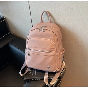 Minimalist dusty pink pebbled leather backpack resting on a design book in a modern setting