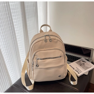 Close-up of beige faux leather backpack with silver zippers on a brown leather surface