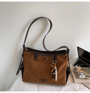 Detail of suede tote bag with leather trim, metal logo plate and ethnic beaded charm