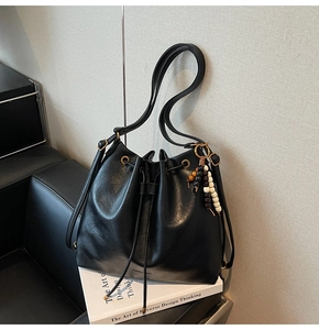 Detail of black drawstring bucket bag with shiny faux leather texture and beaded charm