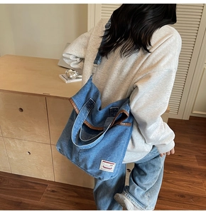 Close-up of denim tote bag featuring brown leather trim and white woven brand label