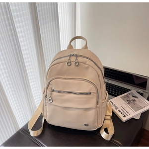 Close-up of beige faux leather backpack with zippers on a desk next to a laptop