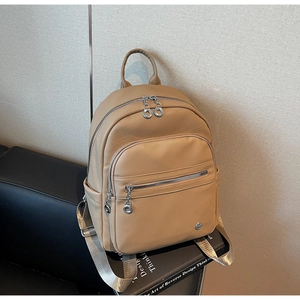 Detail of khaki pebbled leather backpack with silver zippers on a black sofa