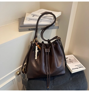 Detailed close-up of dark brown drawstring bucket bag with beaded charm on soft stool
