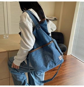 Detail of blue denim tote bag with brown leather trim and red woven tag on model back