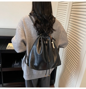 Detail of black pleated bucket backpack with drawstring closure and bead charm on model