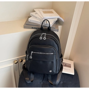 Detail of black lychee leather backpack with silver zippers on a stack of books