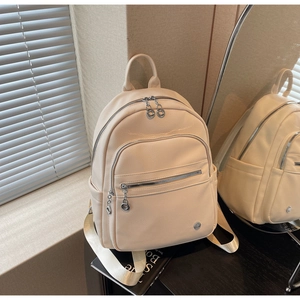 Close-up of beige lychee grain leather backpack with multi-zipper compartments and silver hardware