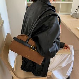 Bruine suède schoudertas met gouden gesp en logo getoond in een minimalistische studio