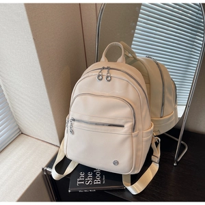 Side view detail of a beige leather backpack with multi-zipper layers and woven straps