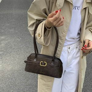 Detail van de donkerbruine baguette-tas met gouden gesp op een stijlvol model in jas