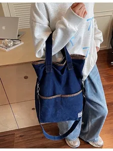 Large blue denim tote bag with brown leather trim and dual straps shown on a model
