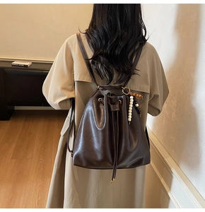 Detail of dark brown bucket bag with beaded charm and drawstring on khaki coat