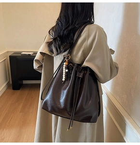 Detailed back view of a dark brown pleated bucket bag worn by a model in a minimal setting