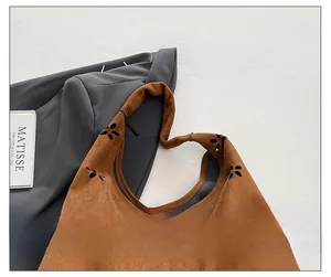 Detail of wide shoulder strap on brown suede tote bag with laser-cut flower patterns