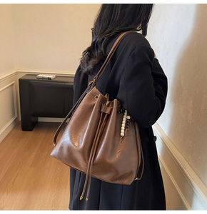 Detail of a large brown pleated bucket bag with adjustable straps and beaded charm