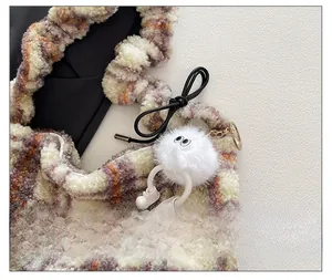 Gros plan d'un porte-clés monstre en peluche blanche sur un sac à main en laine à carreaux