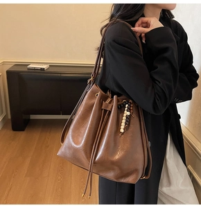 Close-up of brown leather bucket bag with pleated texture and beaded charm detail