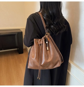 Detail of a brown pleated bucket backpack with drawstring closure and wooden bead charm