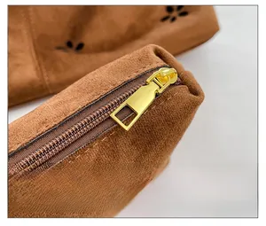 Detail of smooth gold zipper and floral laser cutouts on brown suede tote bag