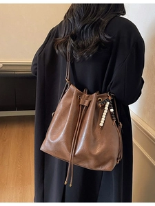Brown pleated bucket bag with drawstring and bead charm shown on a female model