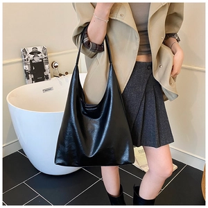 Grand sac hobo noir en similicuir brillant porté avec un trench-coat pour un look de bureau chic