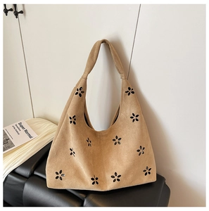 Detailed view of brown suede tote bag with laser-cut floral patterns on a leather sofa