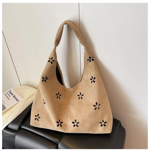 Detailed texture of laser-cut flower pattern on tan suede tote bag on a black chair