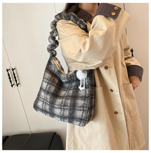 Détail du sac cabas à carreaux gris en peluche avec un pompon doux sur un trench-coat kaki