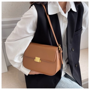 Close-up of a vintage brown leather crossbody bag with a gold buckle worn by a model