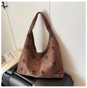 Detail of caramel brown suede hobo bag with laser-cut flower patterns on a sofa