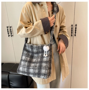 Détail du sac cabas en peluche à carreaux gris et blanc avec un charm pompon sur un mannequin