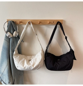 Detail of minimalist nylon crescent crossbody bags in cream and black hanging on wall hooks