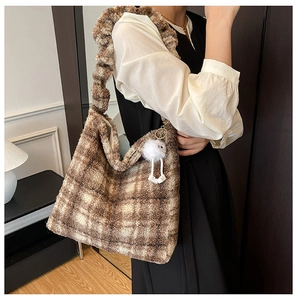 Détail d'un sac hobo à carreaux marron avec un pompon blanc et une bandoulière froncée