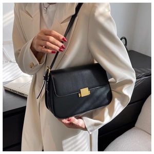 Detail of a black minimalist leather crossbody bag featuring a gold square buckle closure