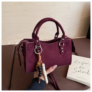 Détail du sac à main bordeaux en daim avec fermeture zippée et breloque en perles