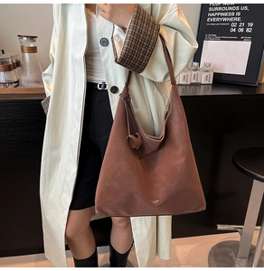 Detail of a large dark brown hobo tote bag worn with a long trench coat in a modern setting