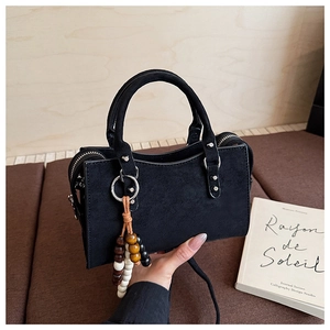 Détail d'un sac à bandoulière en daim noir avec rivets et pendentif pompon à perles colorées
