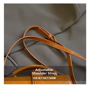 Detail of adjustable shoulder strap with metal buckle on brown textured leather bag