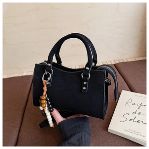Détail du sac à main en daim noir avec pendentif en perles de bois et finitions métal