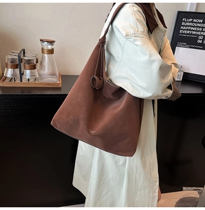 Detail of a large brown suede tote bag carried by a model wearing a beige trench coat
