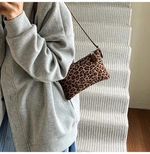 Close-up of leopard print underarm bag with slim brown leather strap worn by model