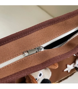 Vue détaillée du sac en toile marron avec écusson de chiot en peluche et fermeture éclair en métal